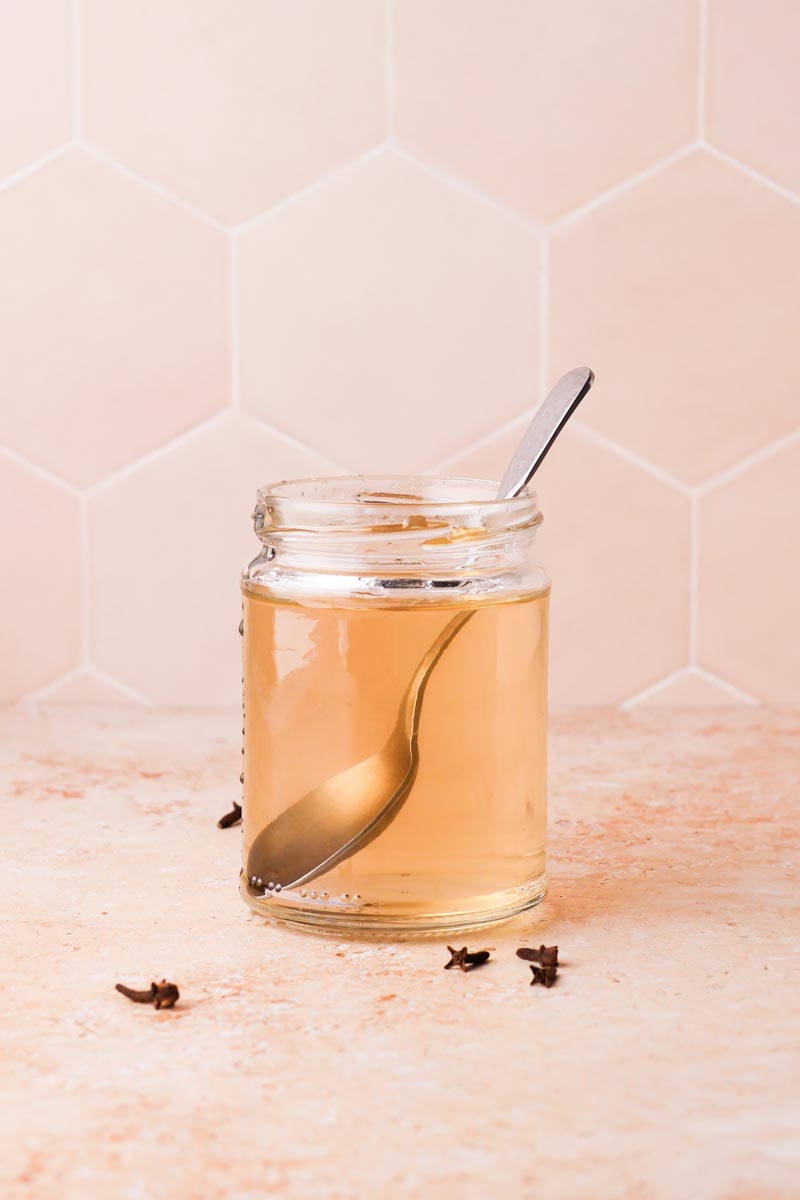 a jar of clove simple syrup with a spoon inside