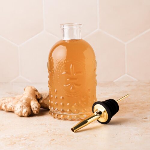 ginger simple syrup in a syrup bottle with ginger pieces beside it