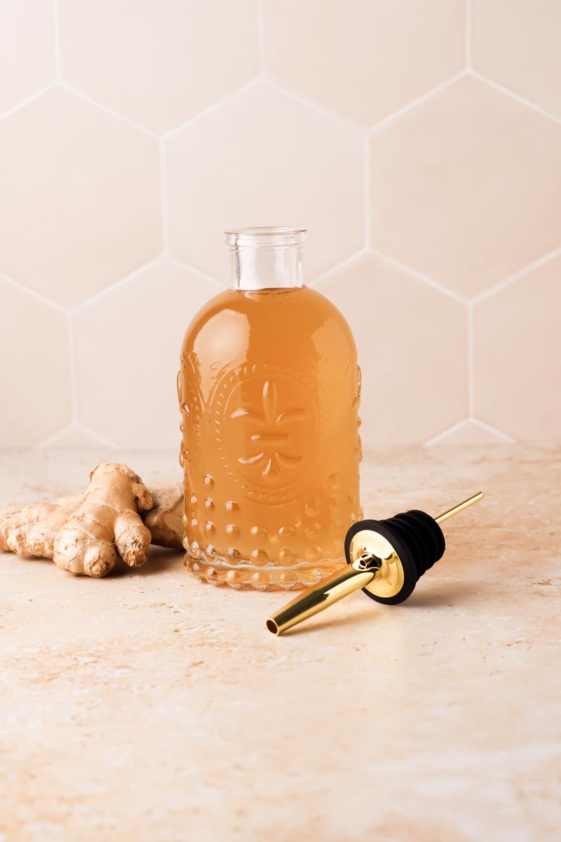 ginger simple syrup in a syrup bottle with ginger pieces beside it