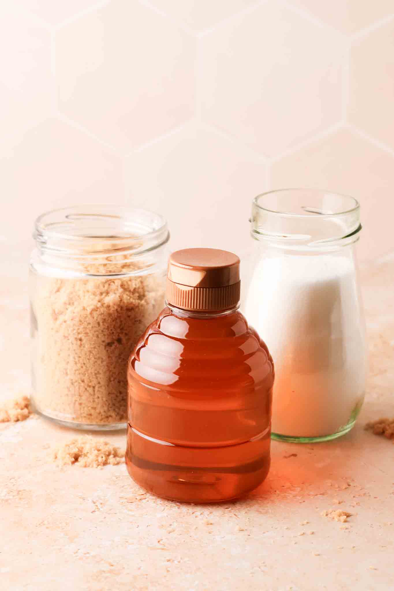 different sugar for syrup : a bottle of honey, white sugar and brown sugar in a glass jar set on a table