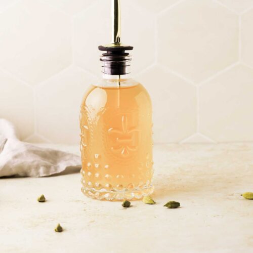 cardamom simple syrup in a bottle with green cardamom seeds scattered around