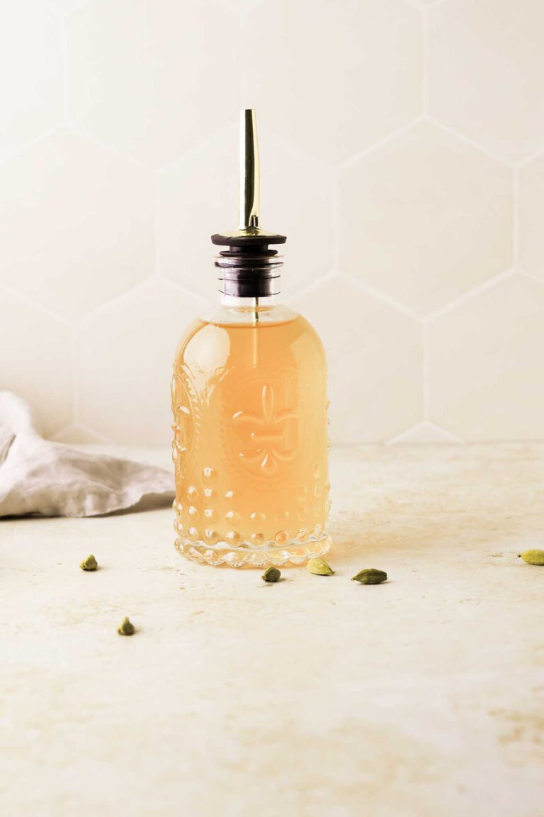 cardamom simple syrup in a bottle with green cardamom seeds scattered around