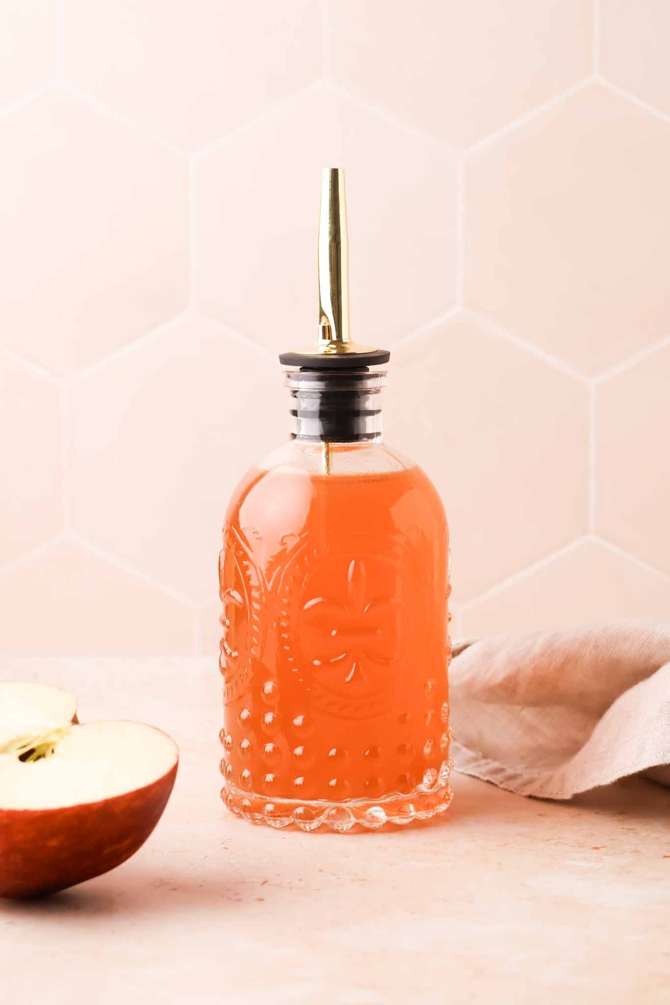 apple cider syrup in a glass bottle sitting on a table, surrounded by sliced apples
