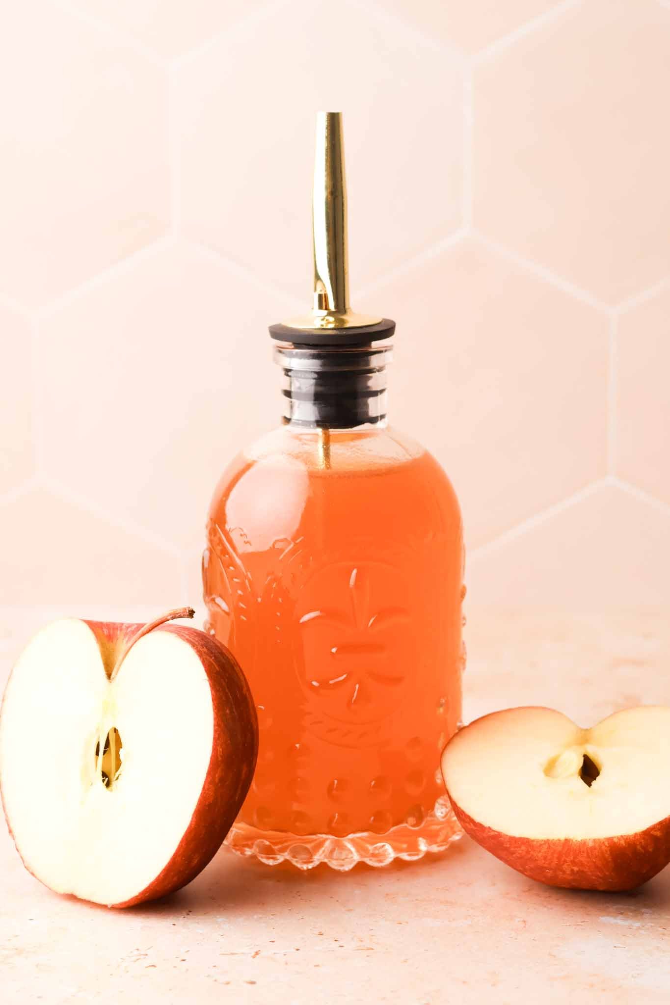 gass bottle of apple cider syrup displayed on a kitchen table with fresh apple halves